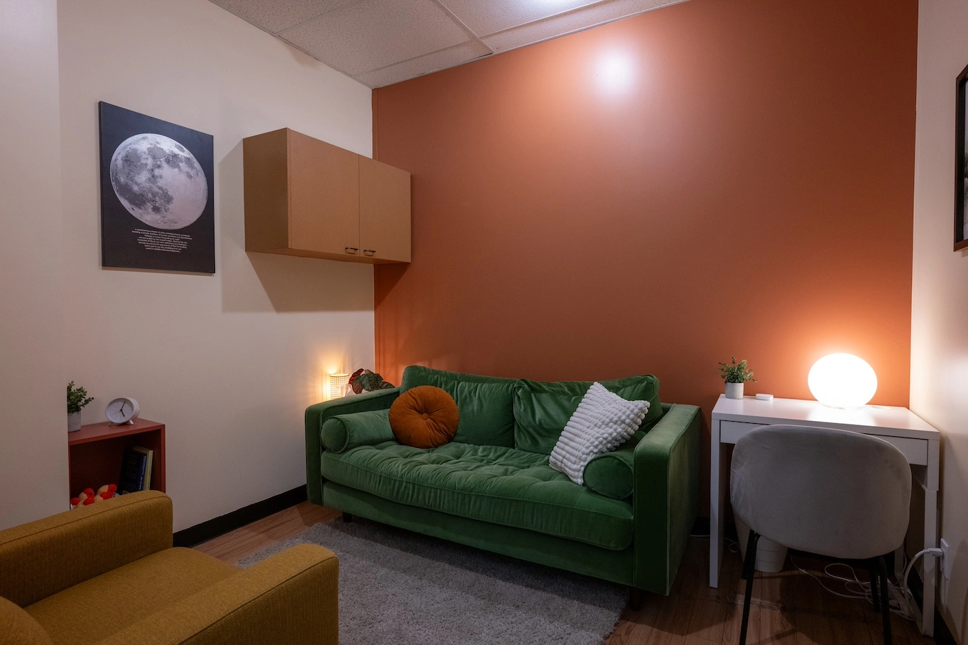 Carly's therapy office in Edmonton: a green sofa against a warm terracotta wall, with soft lamp light